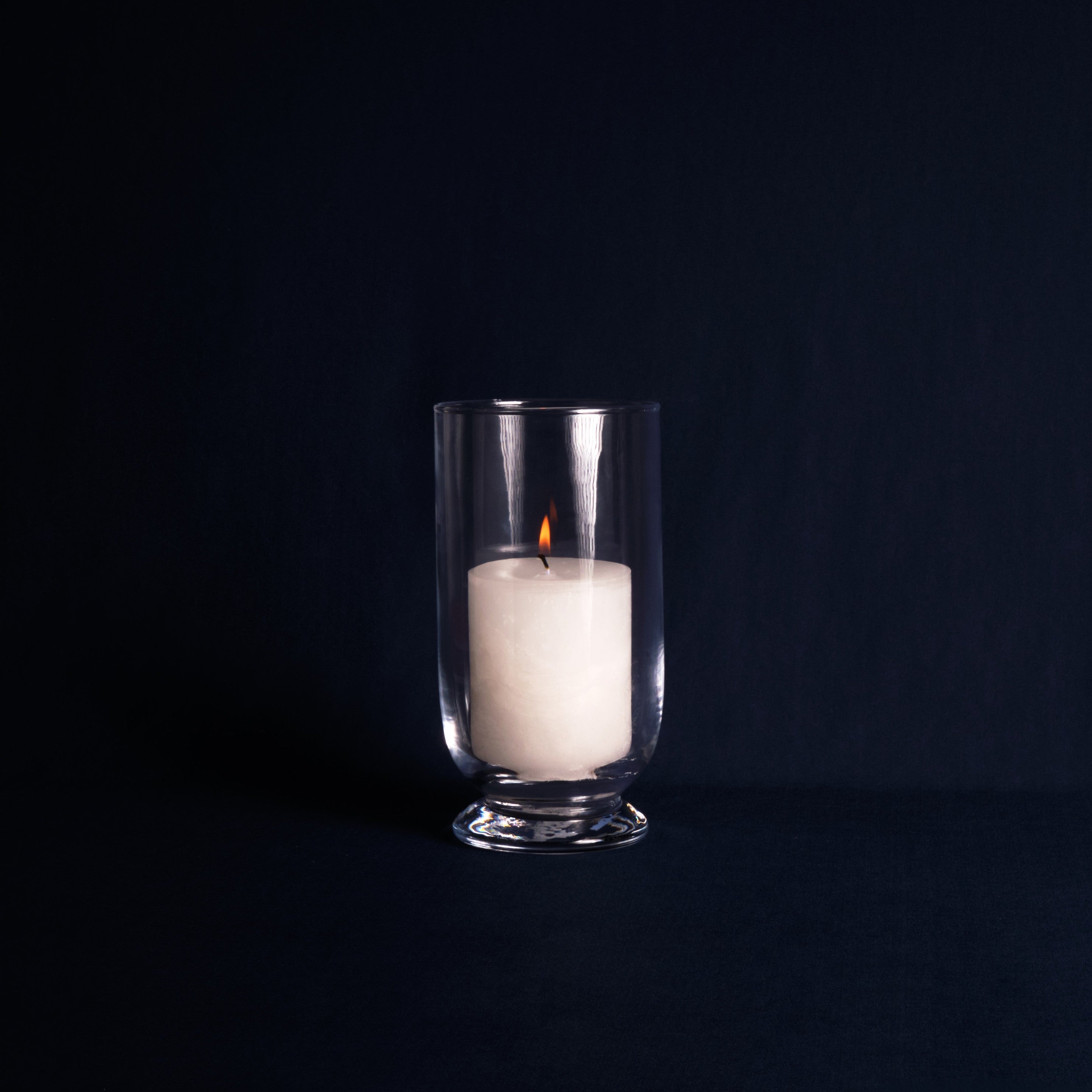 White candle in a clear glass holder on a black background