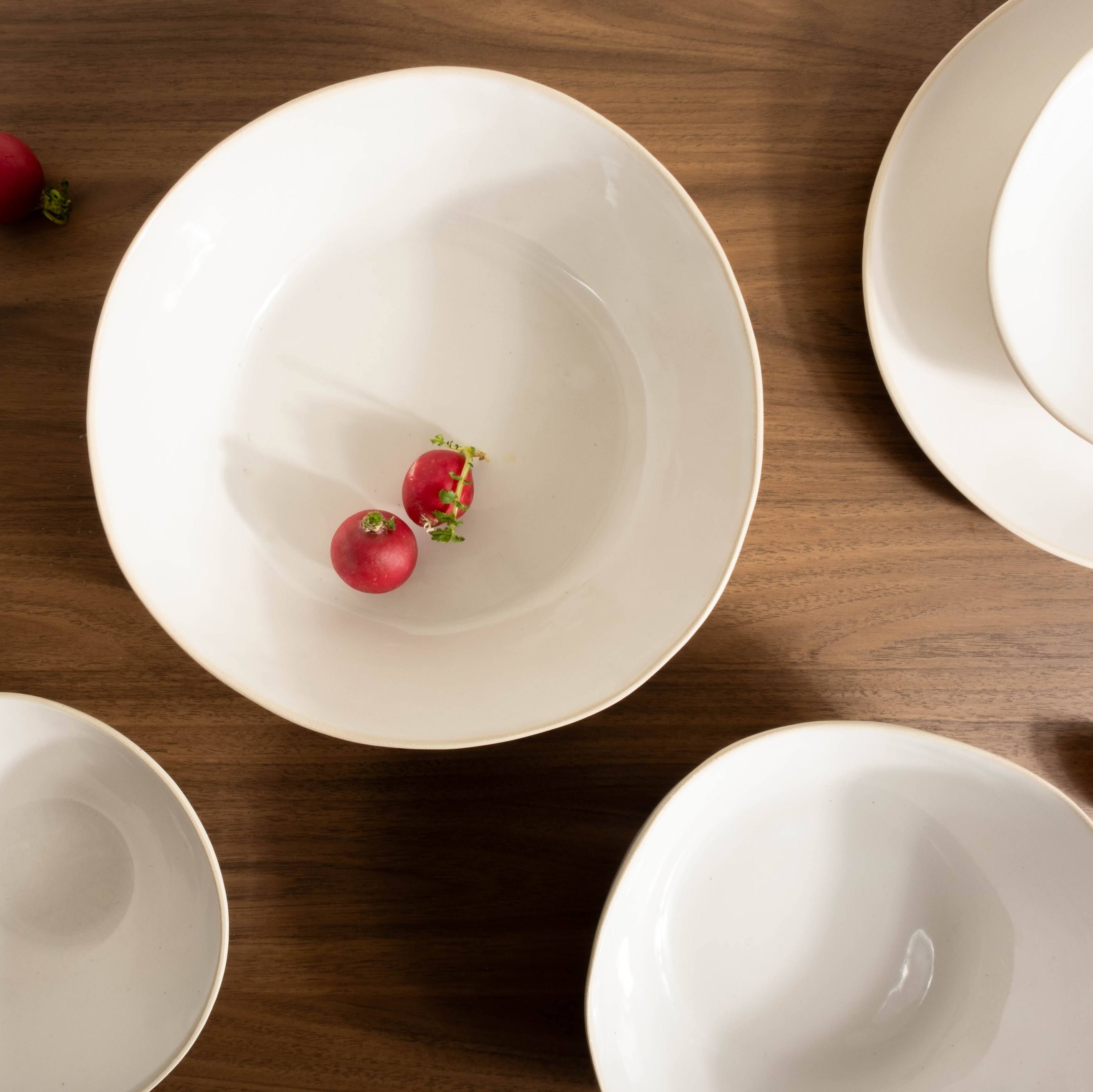 White ceramic bowls on a wooden surface with small red flowers.