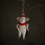 White mouse ornament with red hat and scarf hanging on a branch against a dark background