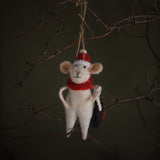 White mouse ornament with red hat and scarf hanging on a branch against a dark background