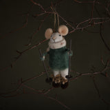 Felted mouse ornament in a green sweater hanging from a branch against a dark background