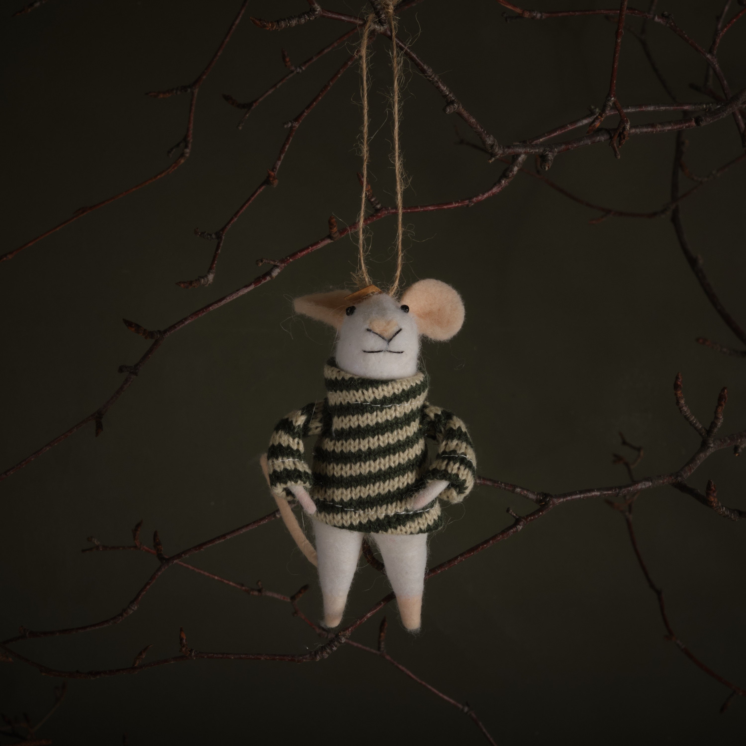 Decorative mouse ornament in a striped sweater hanging from a branch against a dark background