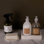 Set of cleaning products including a spray bottle, pump bottles, and a bar of soap on a marble surface.