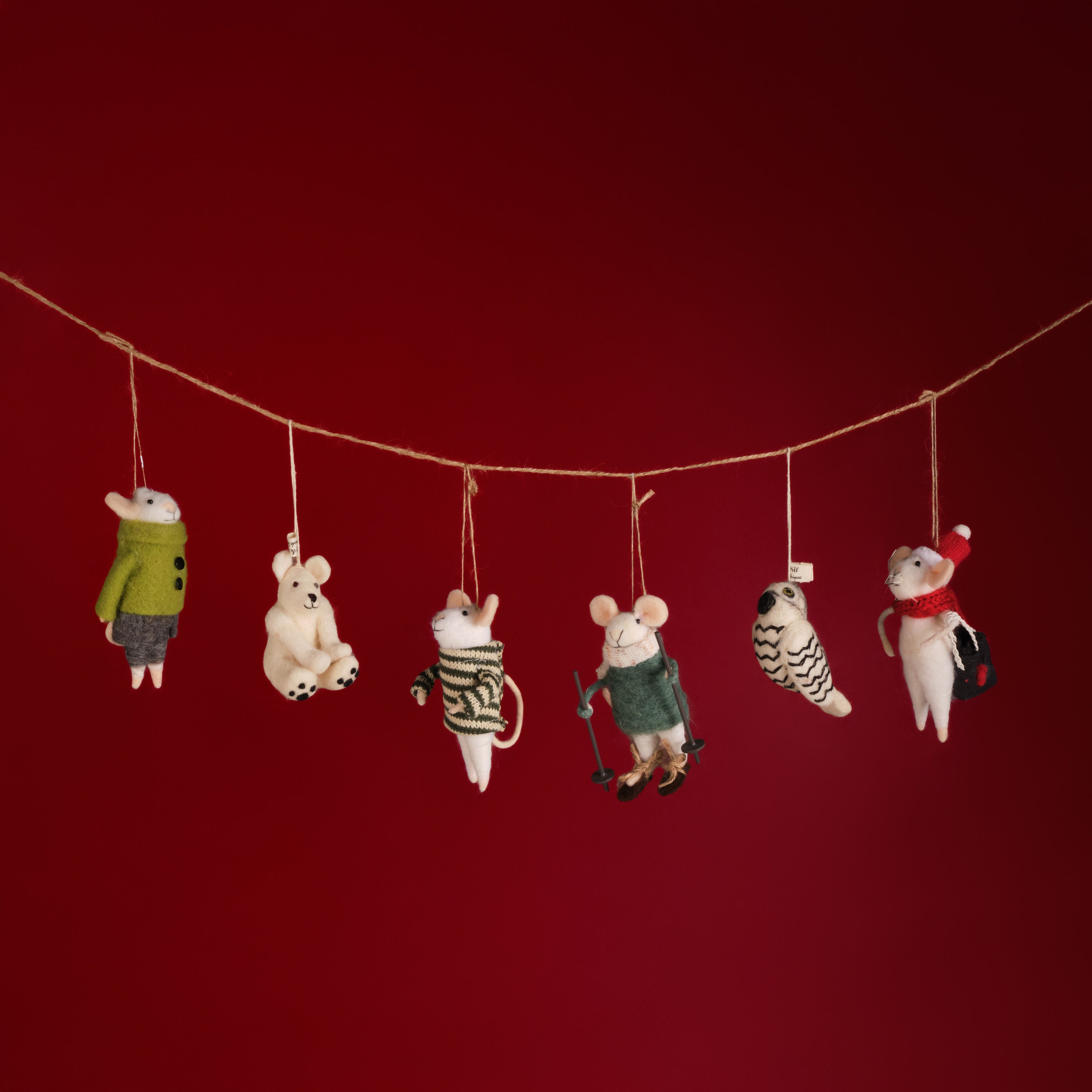 Set of small animal figurines in winter clothing hanging on a string against a red background