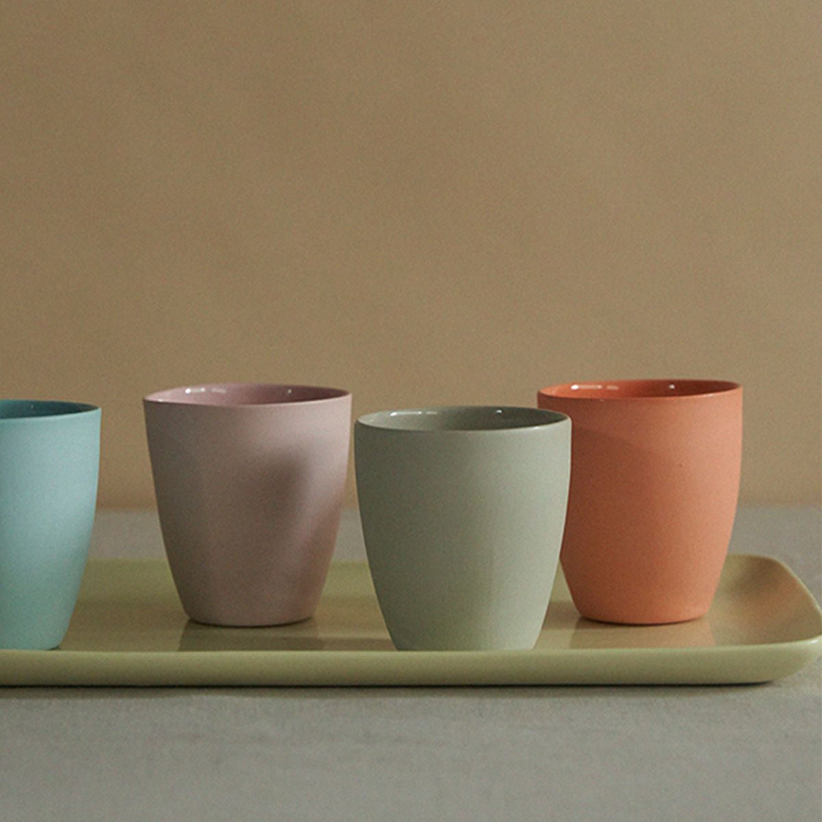 Four colorful ceramic cups on a tray against a beige background
