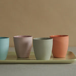 Four colorful ceramic cups on a tray against a beige background