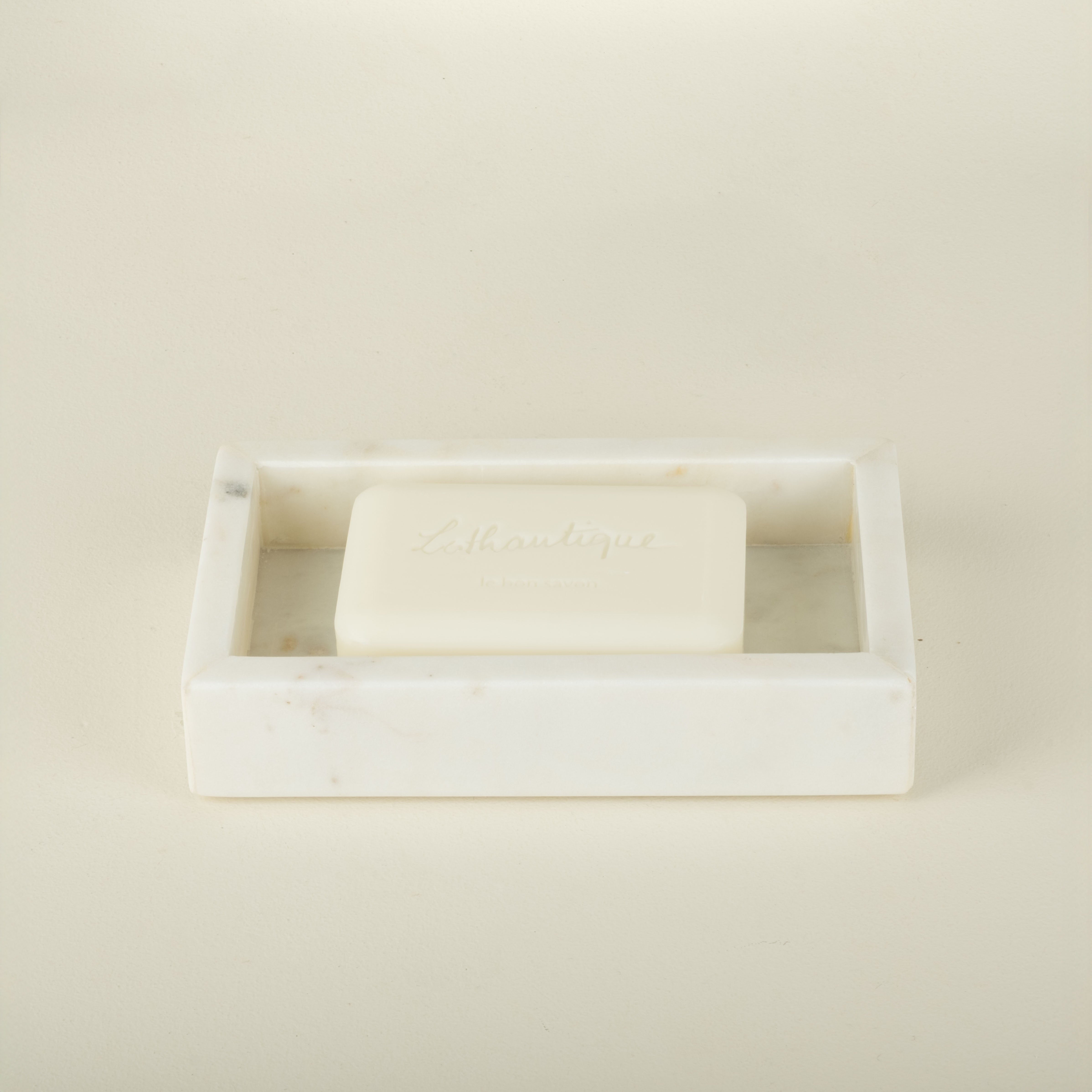 White soap bar in a rectangular soap dish on a beige background