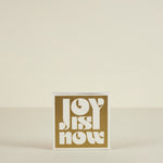 Card with 'Joy is Now' text on a beige background