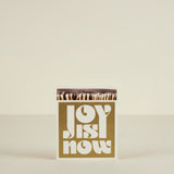Matchbox with 'Joy is Now' text on a beige background