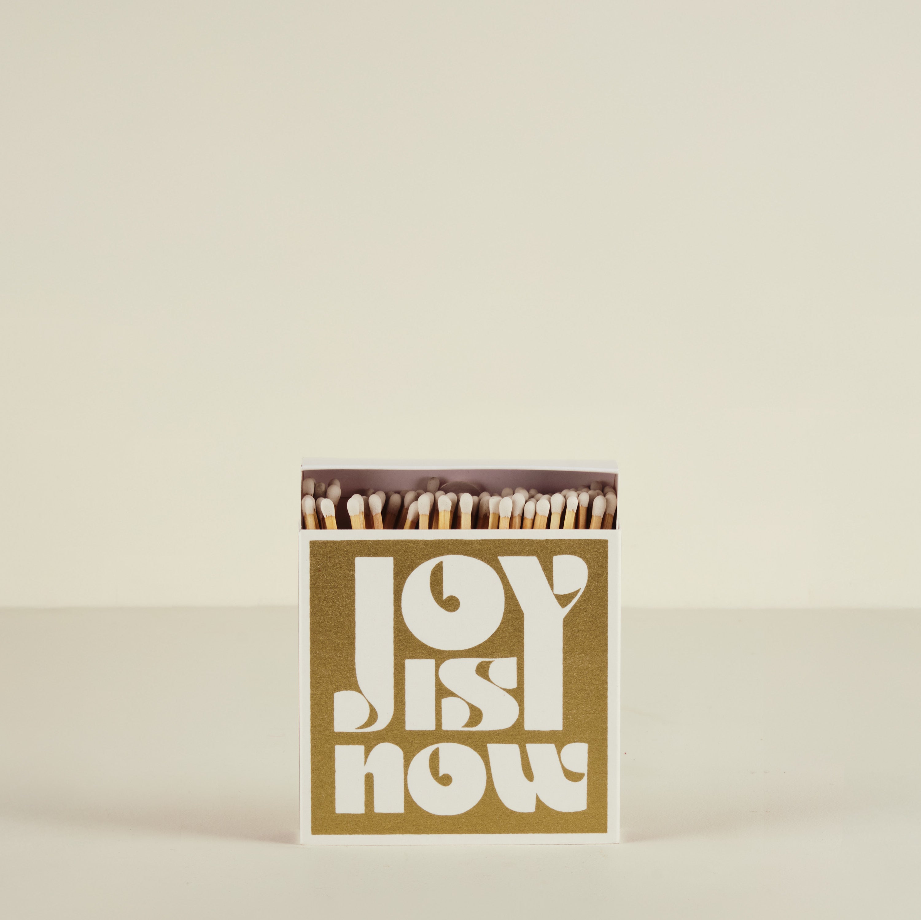Matchbox with 'Joy is Now' text on a beige background