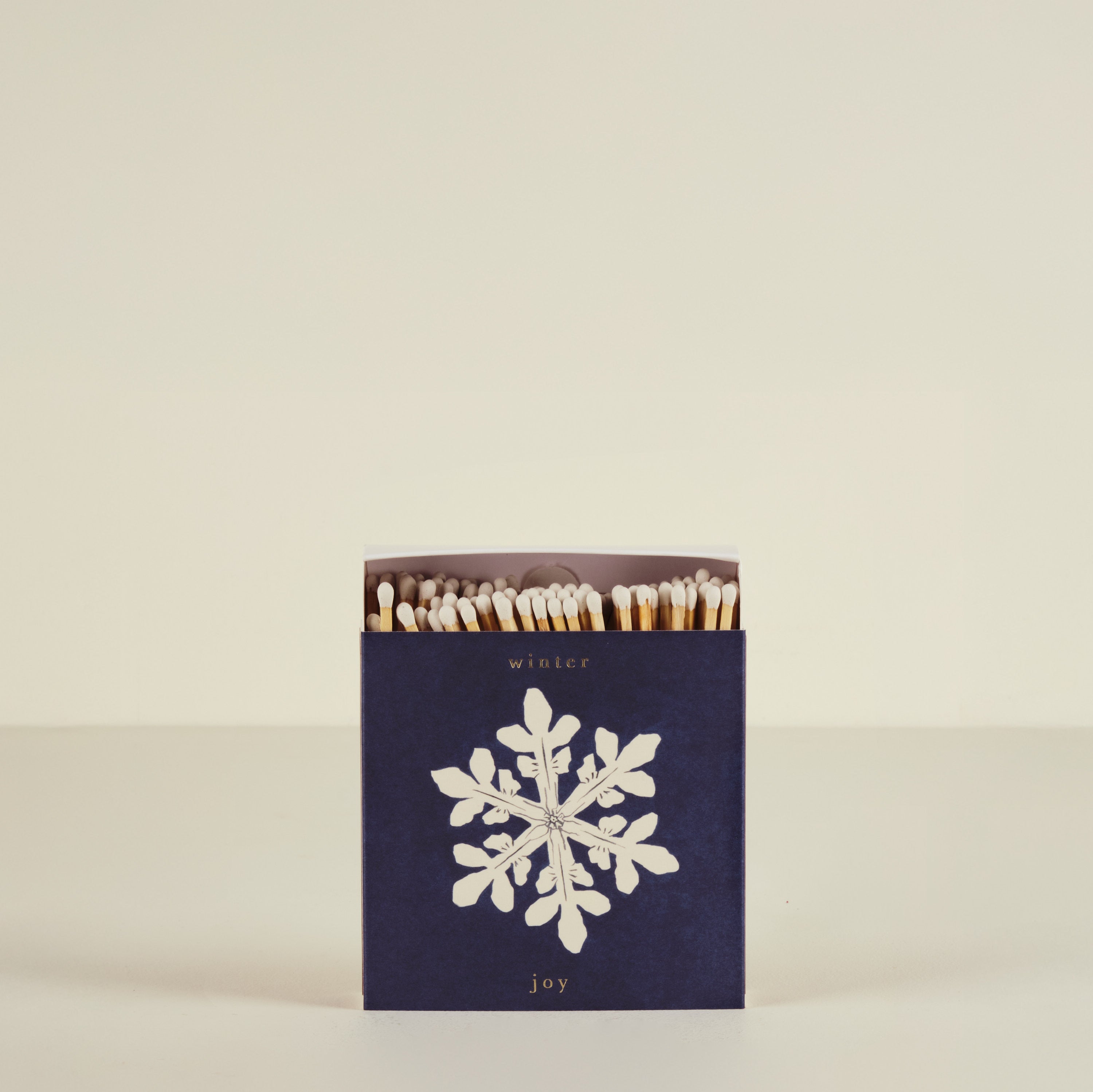 Matchbox with snowflake design and 'winter joy' text on a beige background