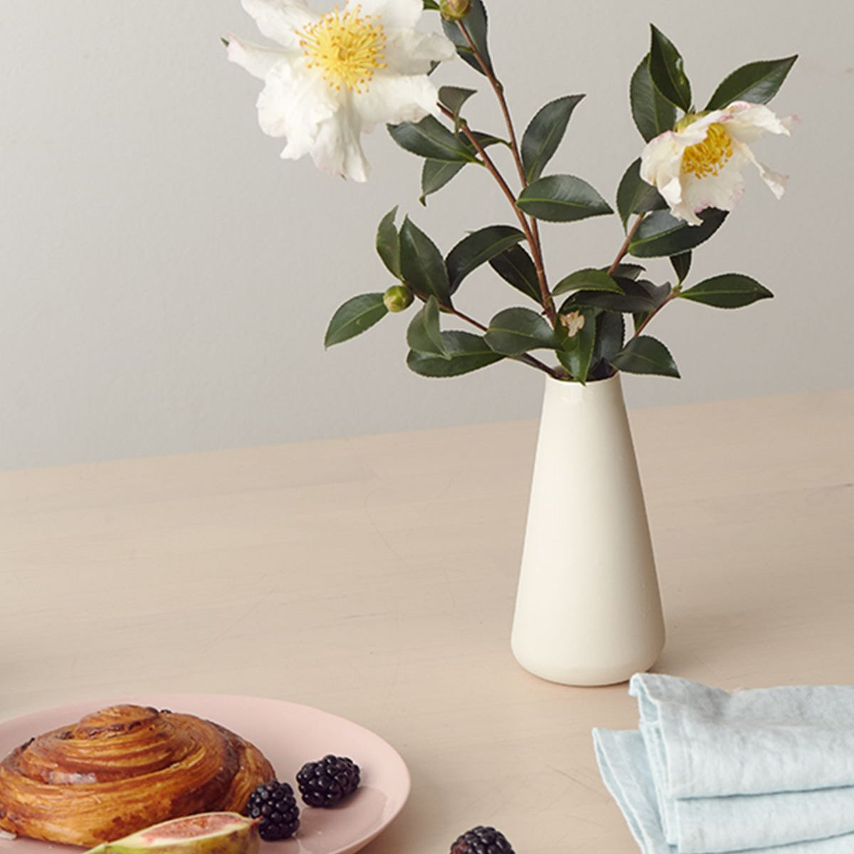 White vase with flowers on a table with pastries and figs
