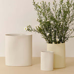 Three white pots on a beige surface with one containing greenery.