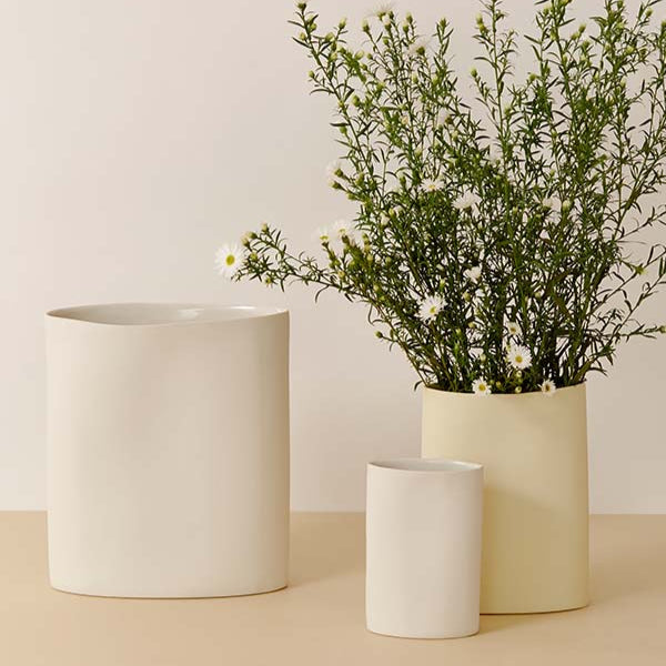 Three white pots on a beige surface with one containing greenery.