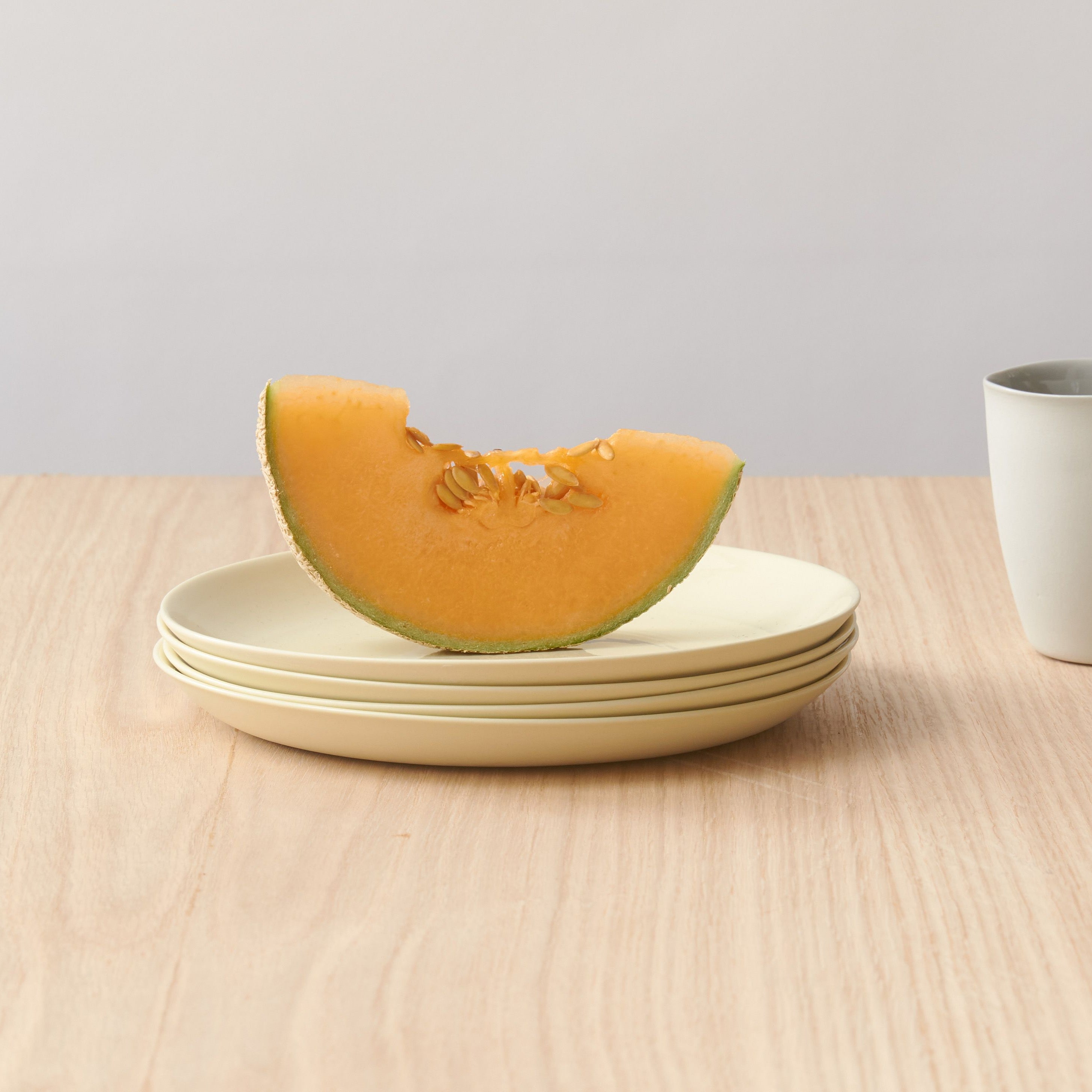 Melon slice on a plate with a cup and utensils on a wooden surface