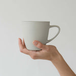 Hand holding a light gray mug against a plain background