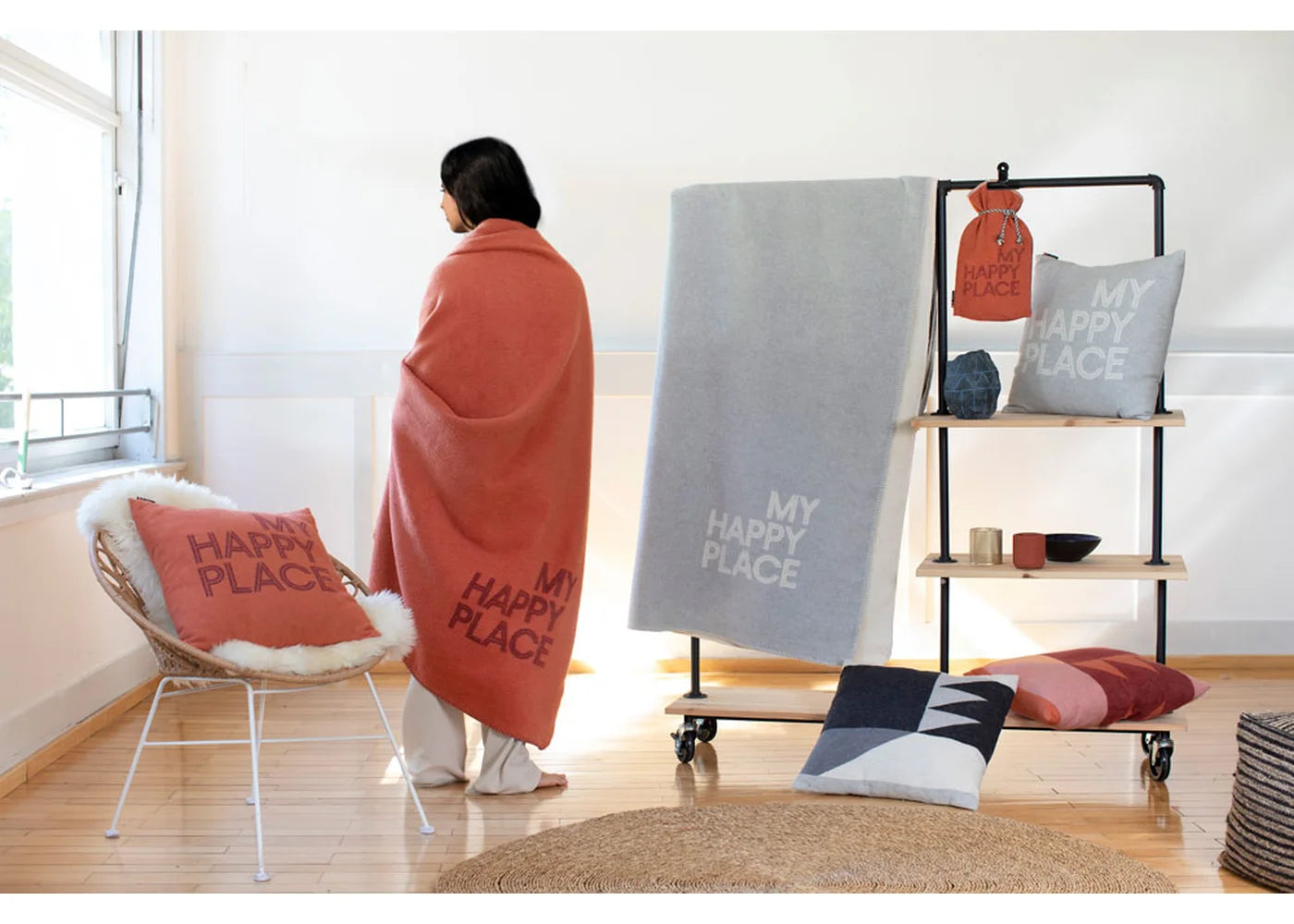Person wrapped in a blanket with 'My Happy Place' text in a room with decorative pillows and a shelf.