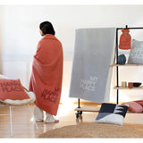 Person wrapped in a blanket with 'My Happy Place' text in a room with decorative pillows and a shelf.
