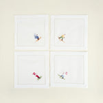 Four white napkins with embroidered skiing designs on a beige background