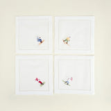 Four white napkins with embroidered skiing designs on a beige background