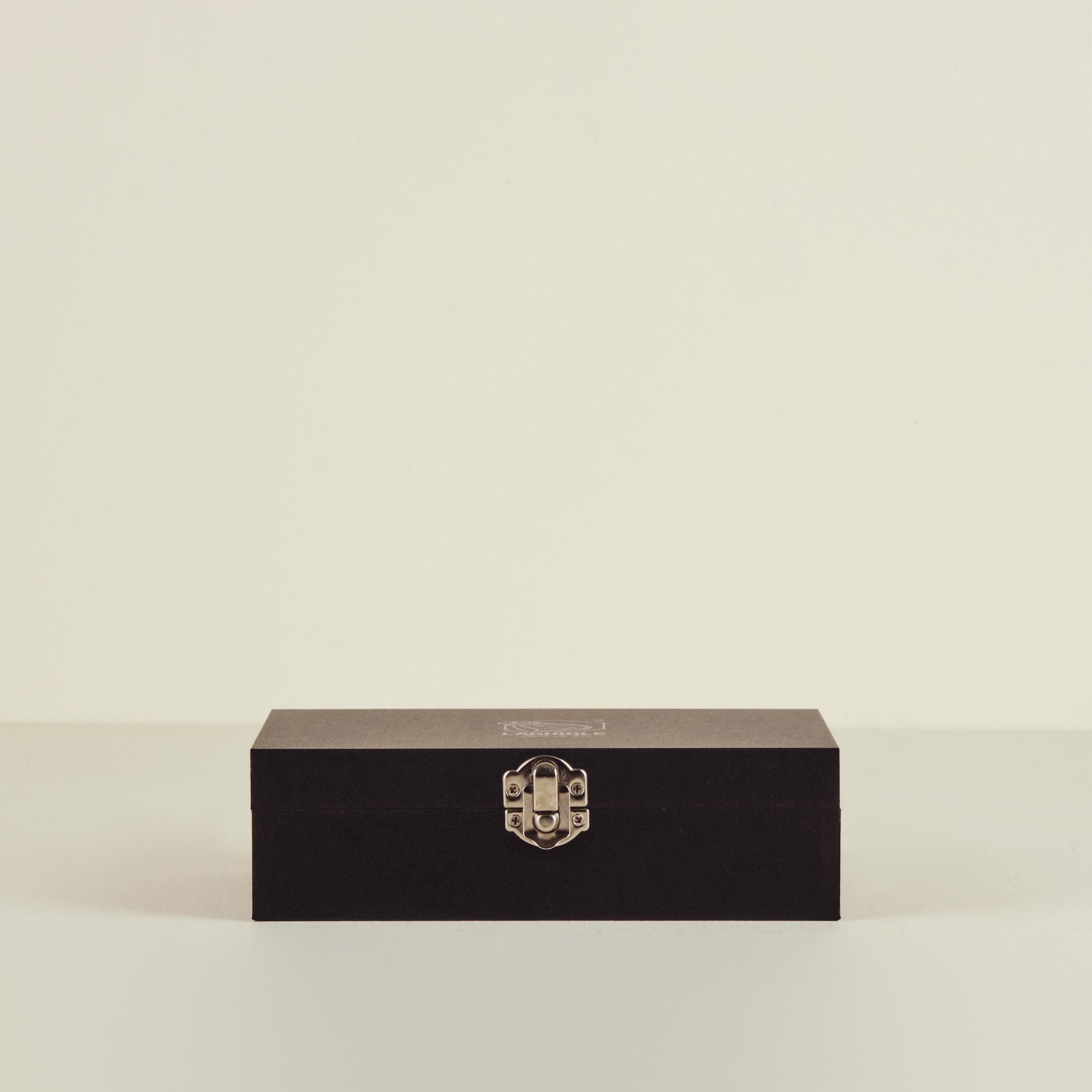 Black rectangular box with a gold emblem on a beige background