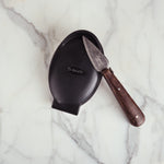 Black ceramic dish with a wooden-handled knife on a marble surface