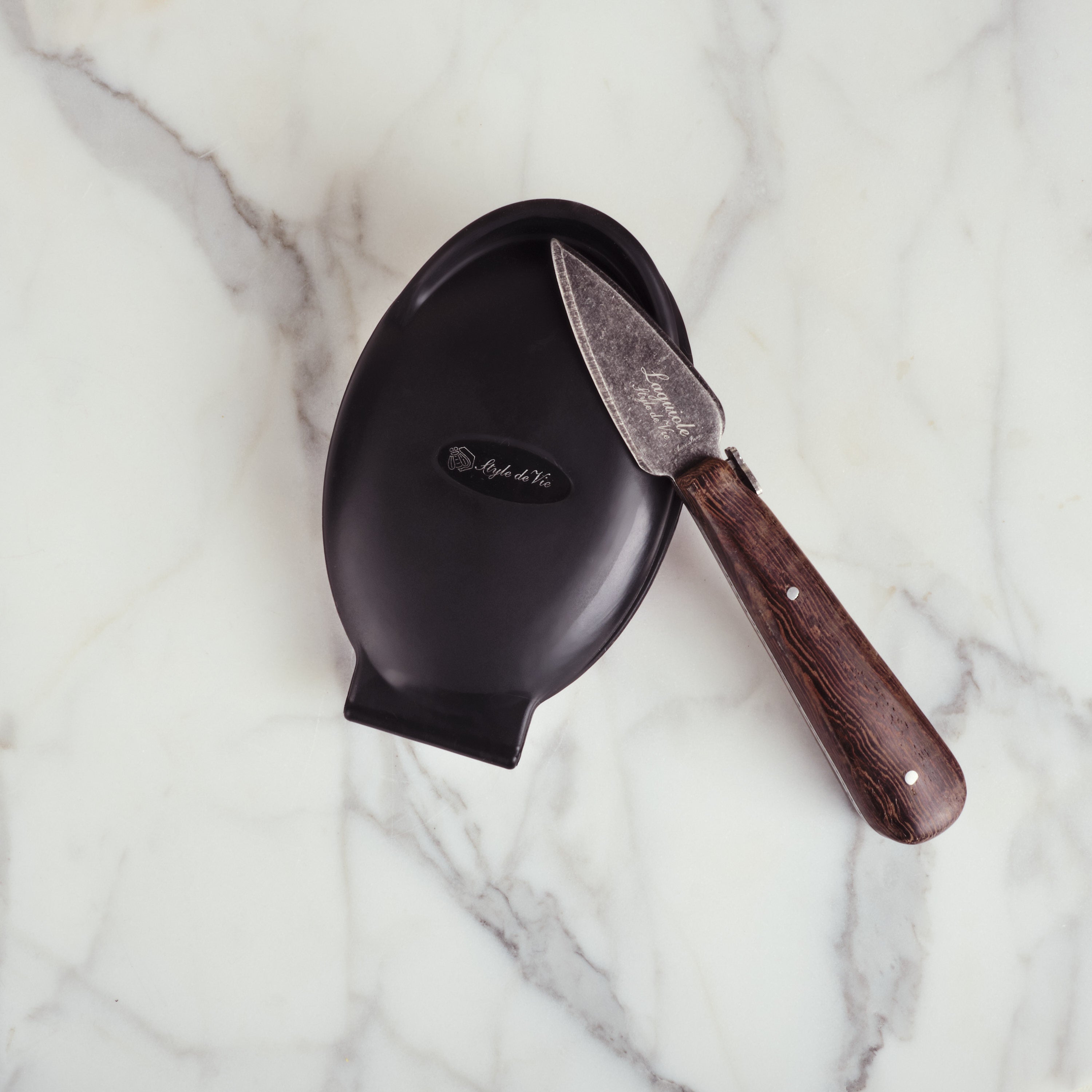 Black ceramic dish with a wooden-handled knife on a marble surface