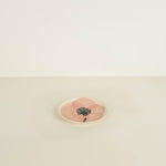 Small round pink stone with a black floral design on a beige background