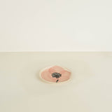 Small round pink stone with a black floral design on a beige background