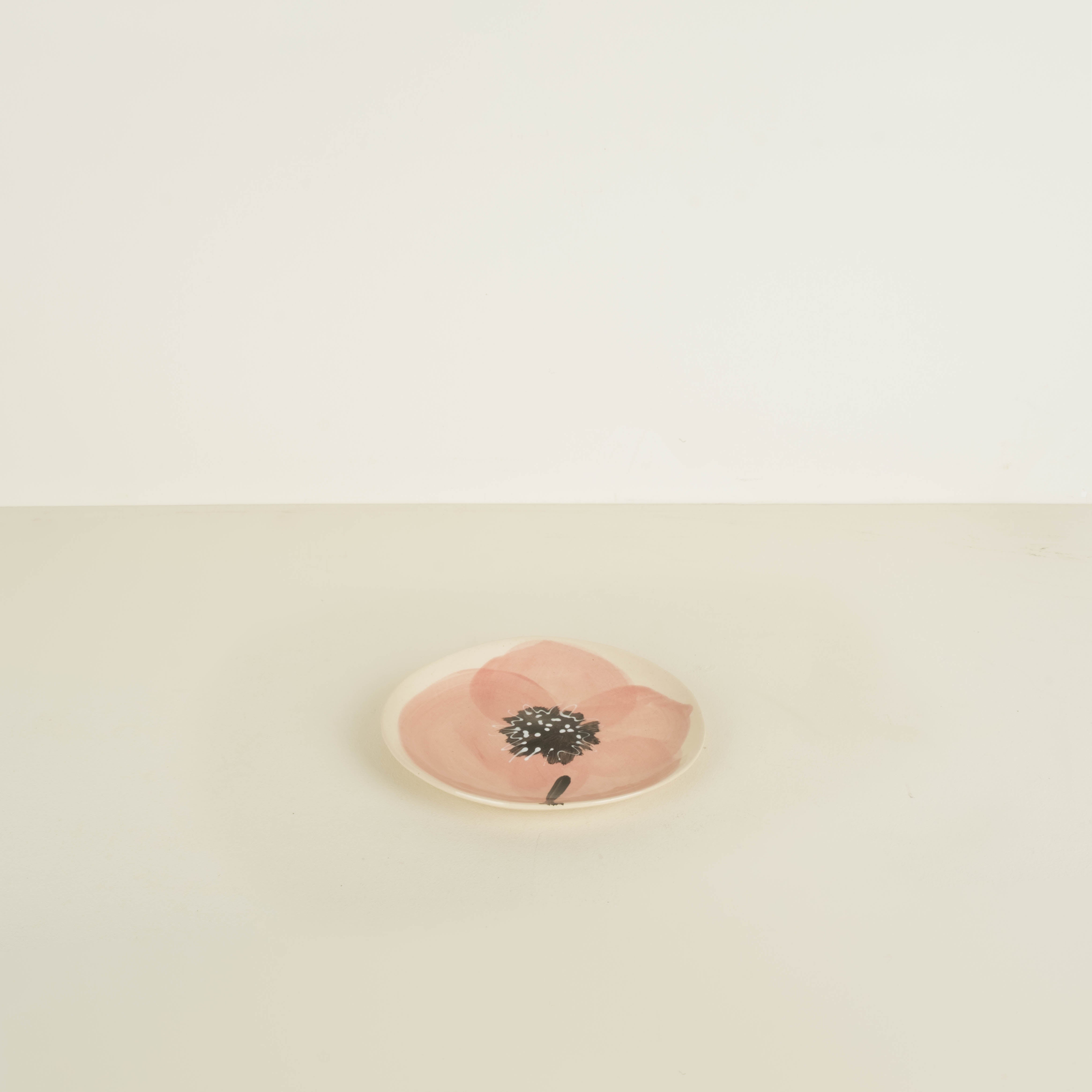Small round pink stone with a black floral design on a beige background