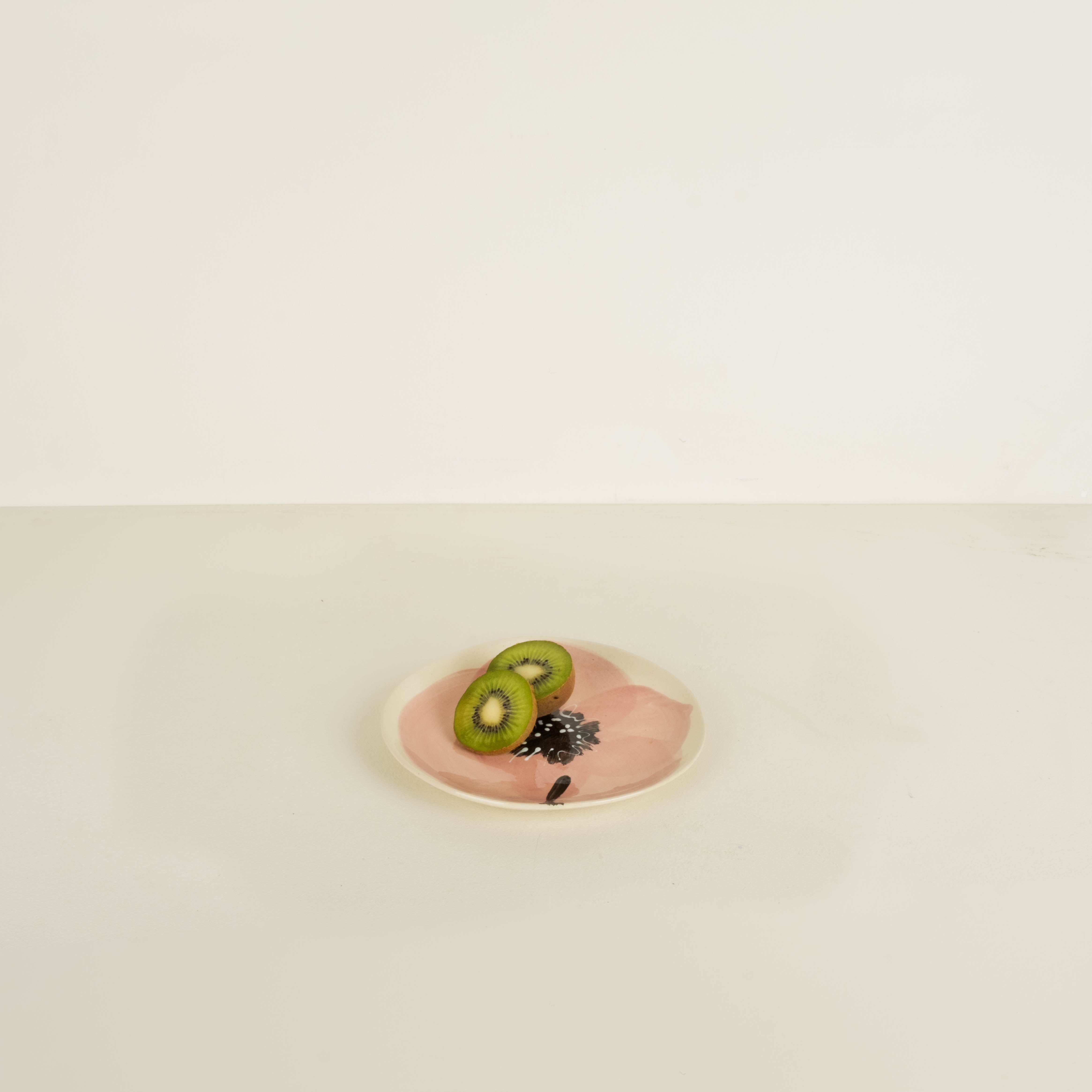 Two kiwi slices on a pink plate with a white background
