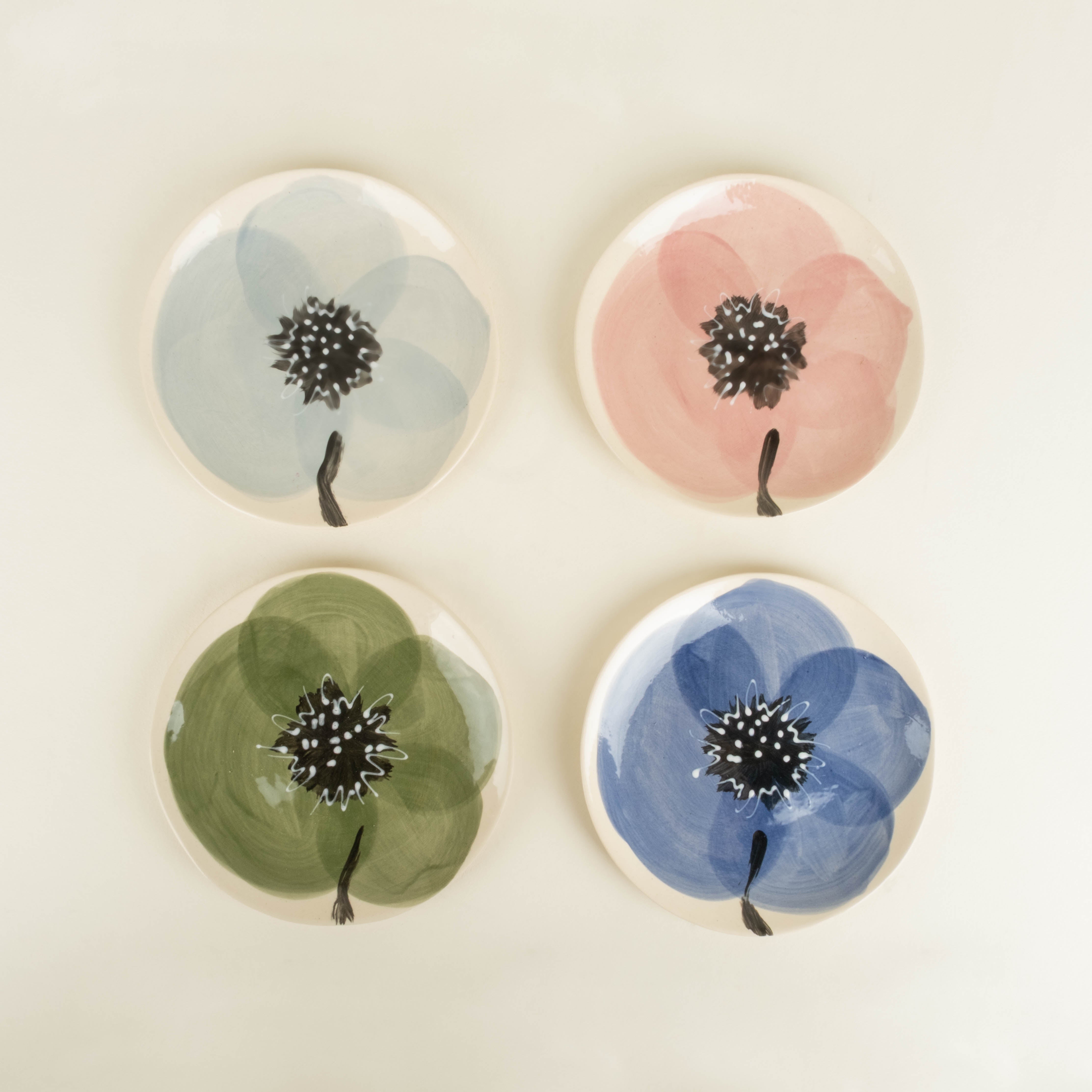 Four round ceramic coasters with floral designs on a beige background