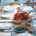 Dining table set for a meal with roasted turkey, vegetables, and wine glasses.