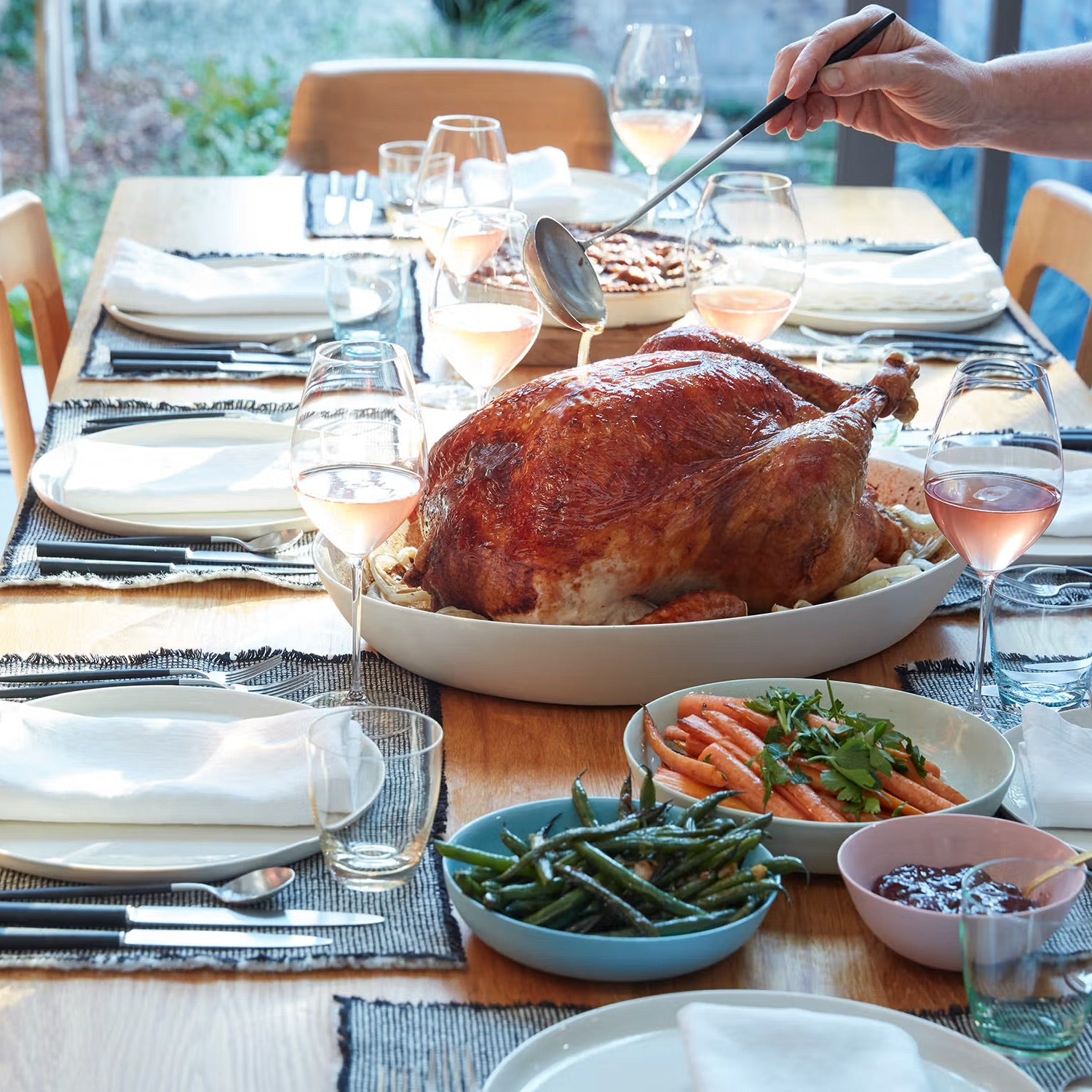 Dining table set for a meal with roasted turkey, vegetables, and wine glasses.