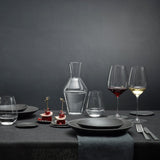 Dining table set with wine glasses, decanter, and black plates on a dark background