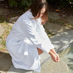 Person in a white robe sitting by a stream outdoors