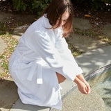 Person in a white robe sitting by a stream outdoors
