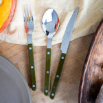 Set of cutlery with green handles on a wooden surface