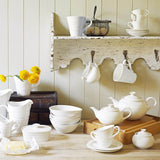 White ceramic tea set on a wooden surface with a rustic shelf in the background.