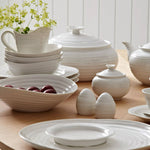 Set of white ceramic tableware including bowls, plates, and teapots on a wooden surface.