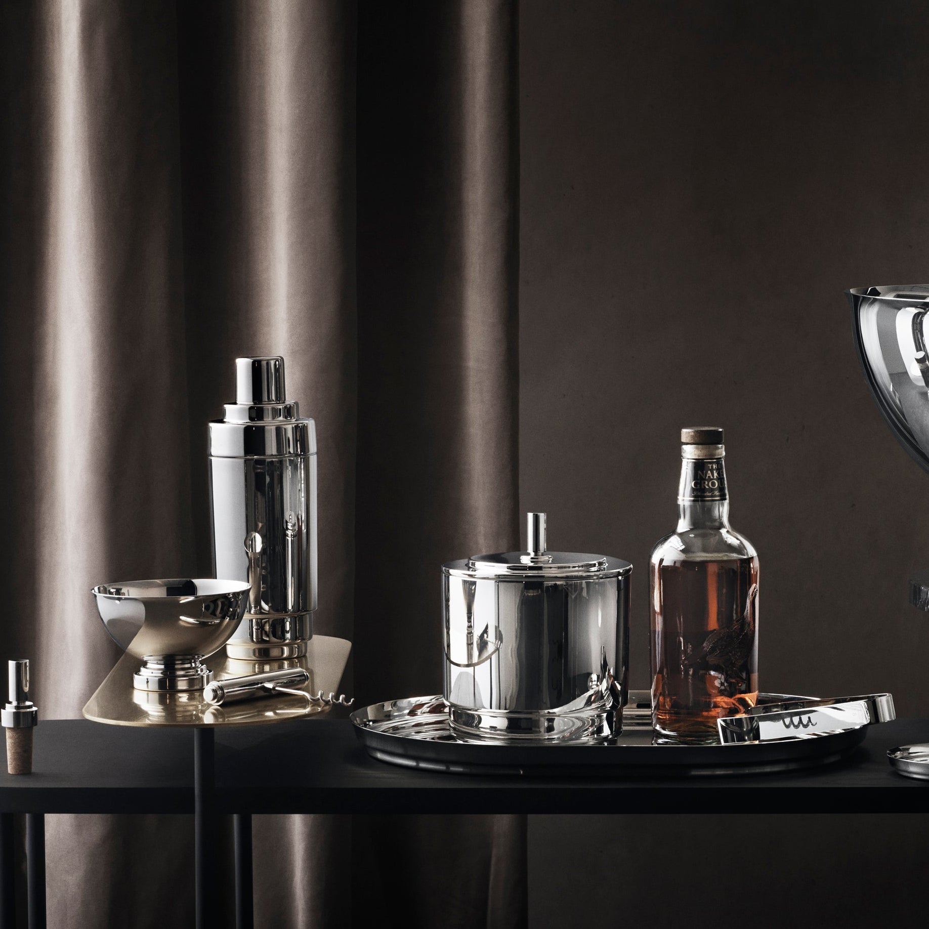 Modern bar setup with cocktail shaker, bottles, and glassware on a dark surface.
