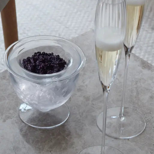 Two champagne flutes with a small bowl of black caviar on a textured surface.