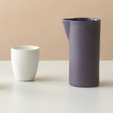 Two white ceramic cups and a purple pitcher on a beige background