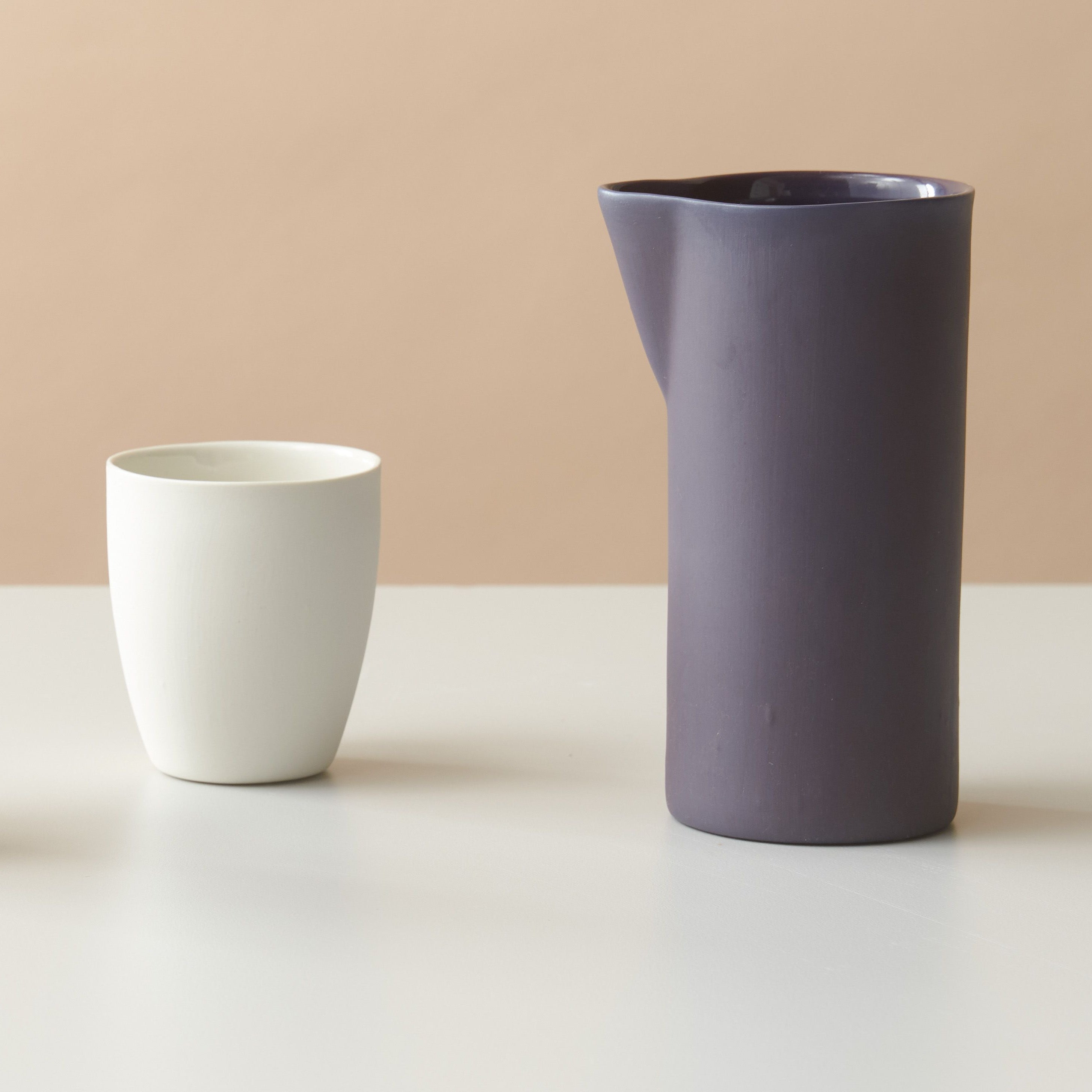 Two white ceramic cups and a purple pitcher on a beige background
