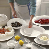 Person preparing seafood dishes on a table with various white ceramic items.