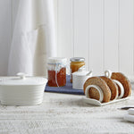 Biscuit holder with cookies on a table next to jars of jam.