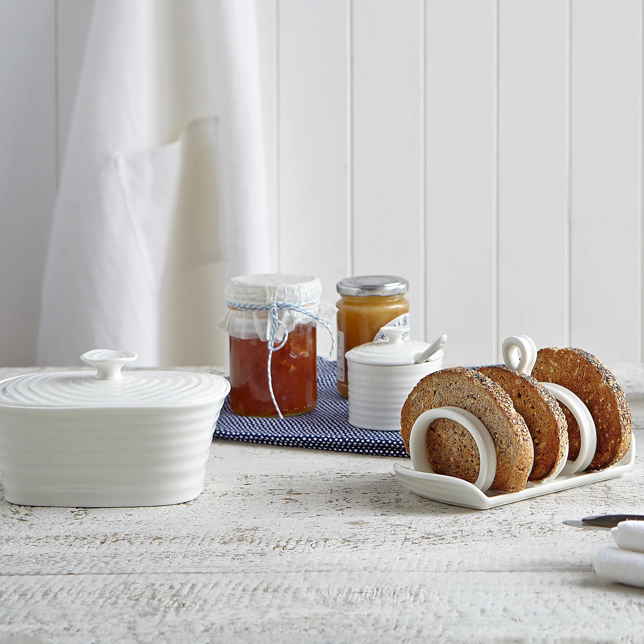 Biscuit holder with cookies on a table next to jars of jam.