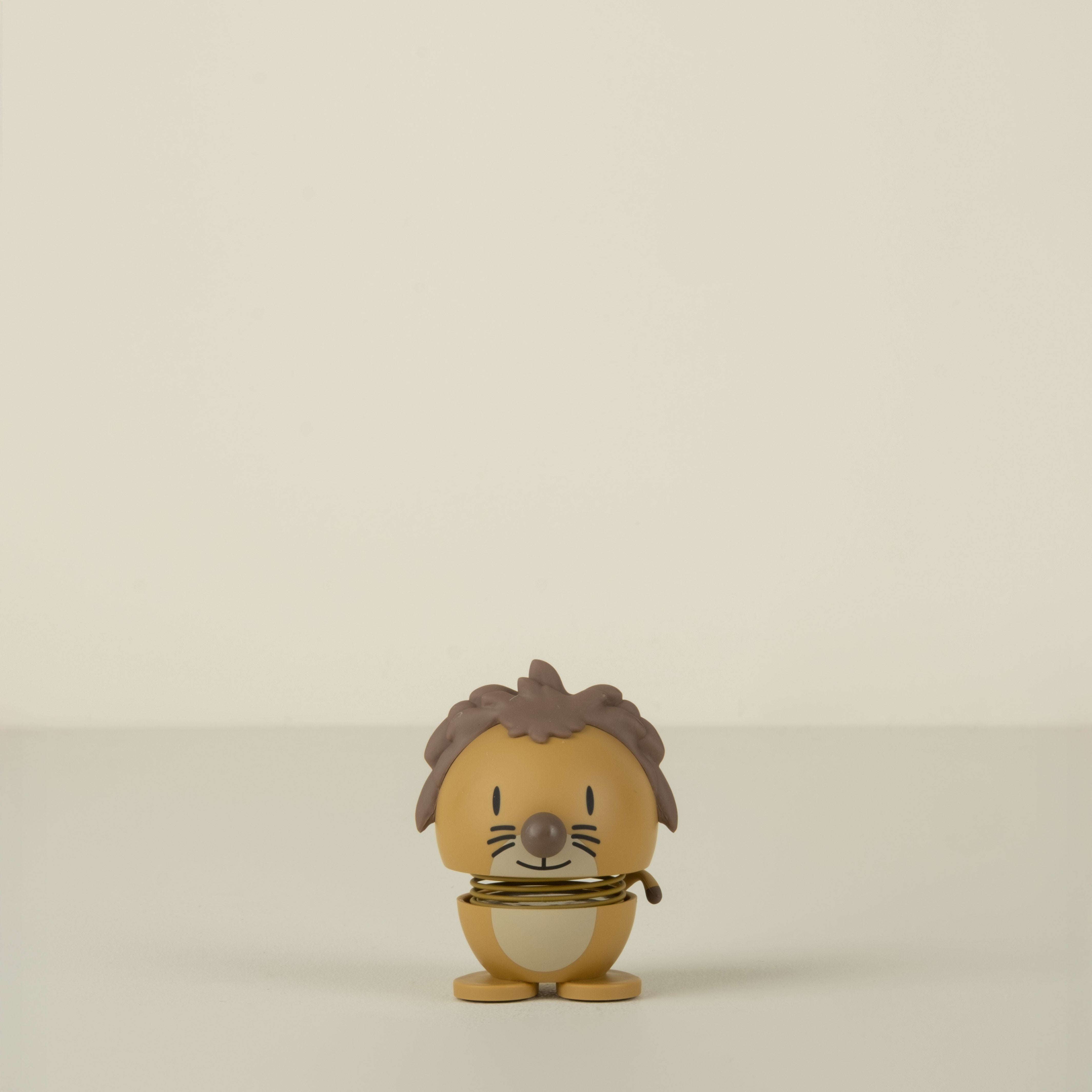 Small figurine of a lion character with brown hair and a yellow outfit on a beige background