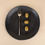 Black plate with a fork and three olives on a beige background