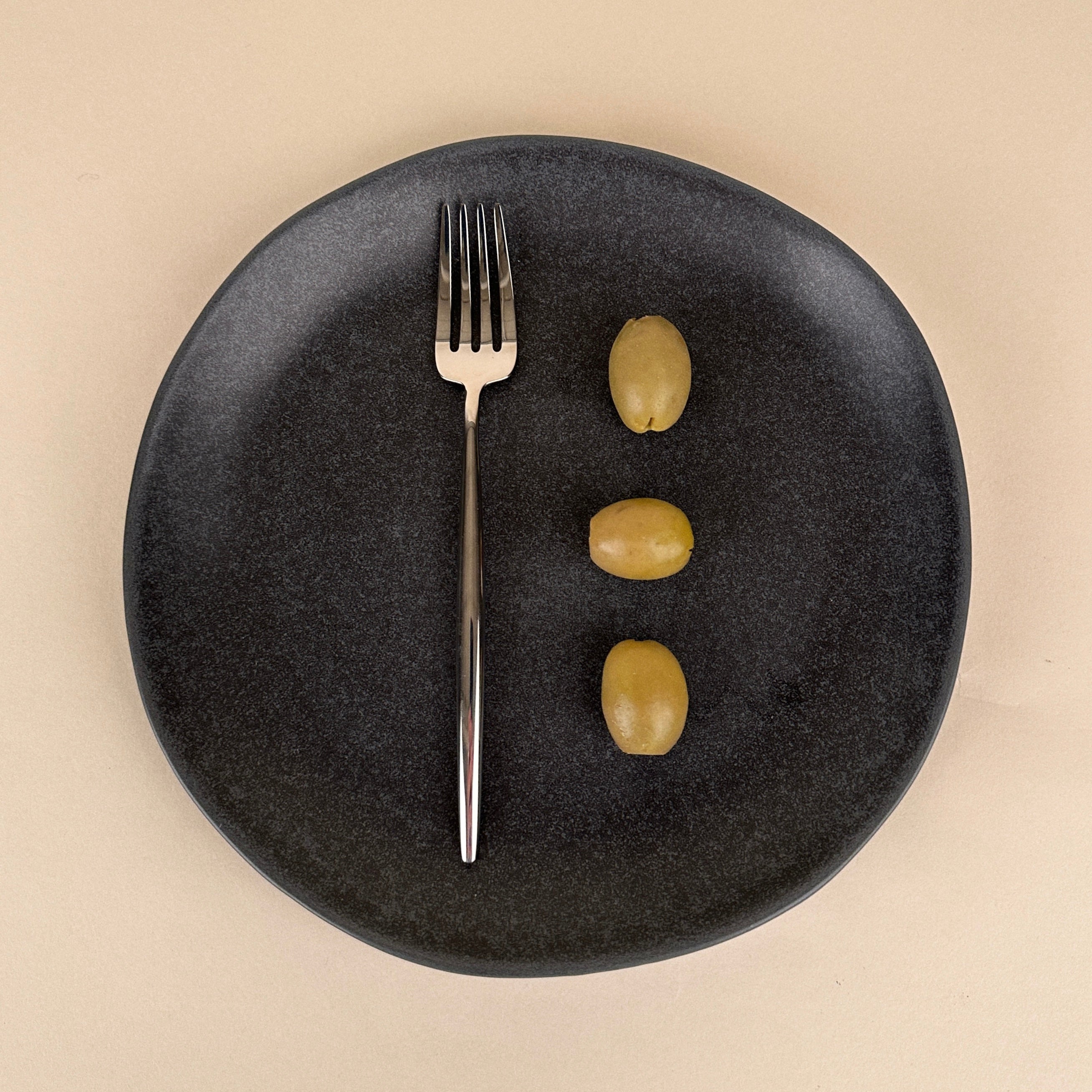 Black plate with a fork and three olives on a beige background